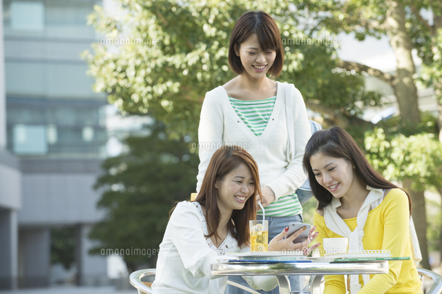 キャンパスのカフェテリアでスマホを見る女子大生三人 の写真素材 イラスト素材 アマナイメージズ