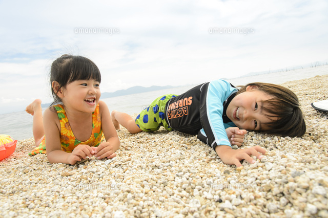 海辺の砂浜でうつ伏せになる水着の子供[10264007039]の写真・イラスト