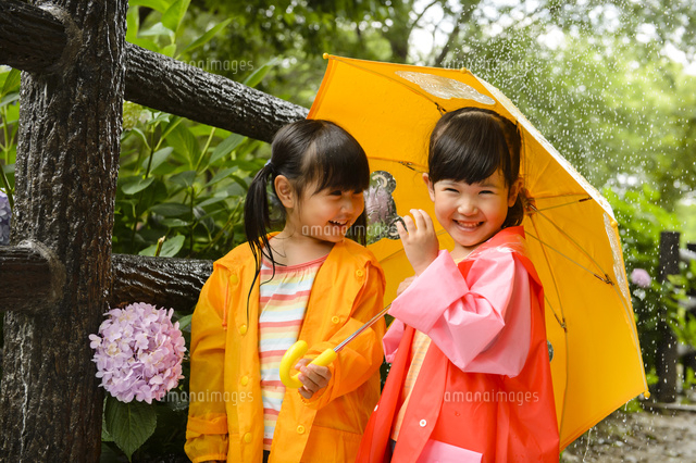 新緑の公園で傘をさして並んでいるレインコートを着た女の子 の写真素材 イラスト素材 アマナイメージズ