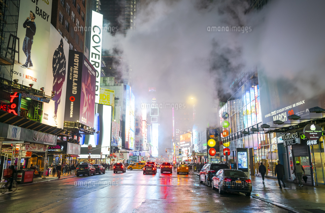 雨の夜にタイムズスクエアのイルミネーションに照らされ輝き漂う蒸気の中を行き交う人々と交通 の写真素材 イラスト 素材 アマナイメージズ