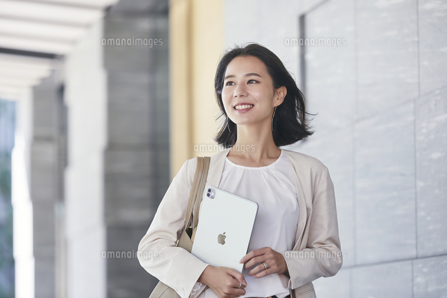 タブレット端末を持ちオフィス街を歩く若い女性 の写真素材 イラスト素材 アマナイメージズ