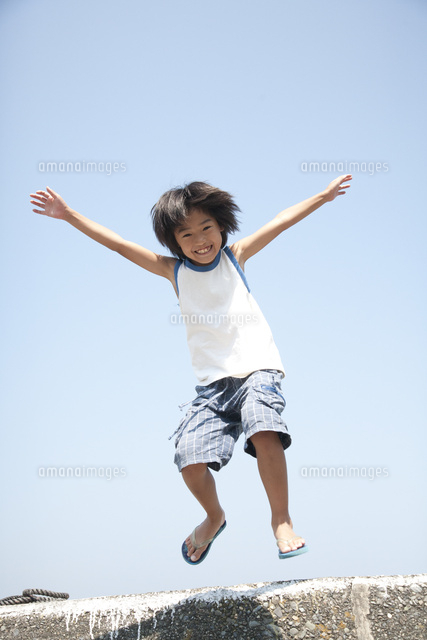 海のそばの防波堤でジャンプして遊ぶ笑顔の男の子 の写真素材 イラスト素材 アマナイメージズ