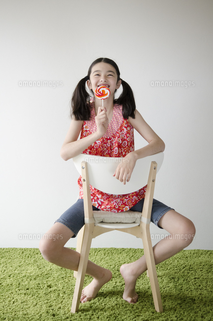 ペロペロキャンディーを持って椅子に座るハーフの少女[10568000464]の