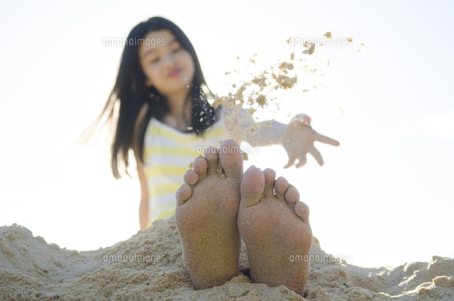 ビーチで砂を自分の足に掛ける女の子 の写真素材 イラスト素材 アマナイメージズ