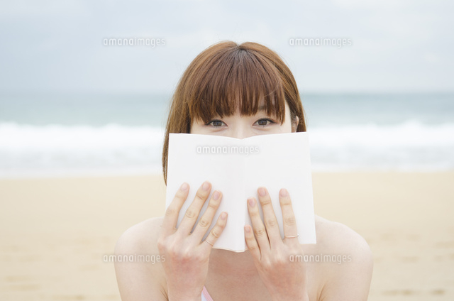 ビーチに座って本で顔を隠す女性 の写真素材 イラスト素材 アマナイメージズ