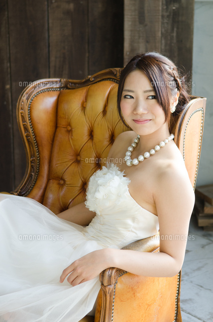 白いドレスを着てソファに座る女性[10568002684]の写真・イラスト素材