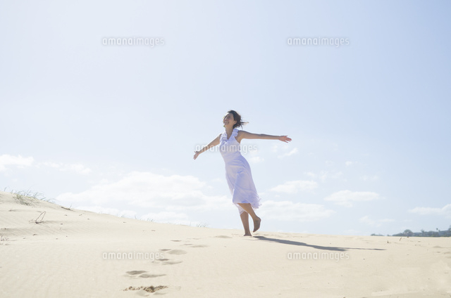 砂の上を手を広げて歩くドレス姿の女性 の写真素材 イラスト素材 アマナイメージズ