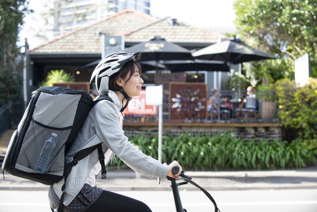 自転車に乗ったフードデリバリーの配達員の後ろ姿 の写真素材 イラスト素材 アマナイメージズ