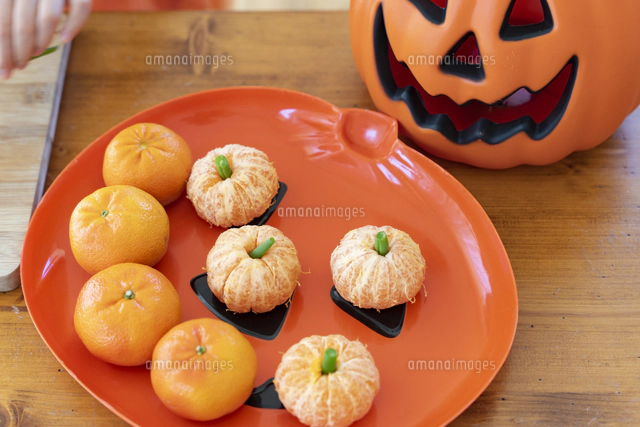 ハロウィンのコスチュームを着てみかんでできたかぼちゃを持っている