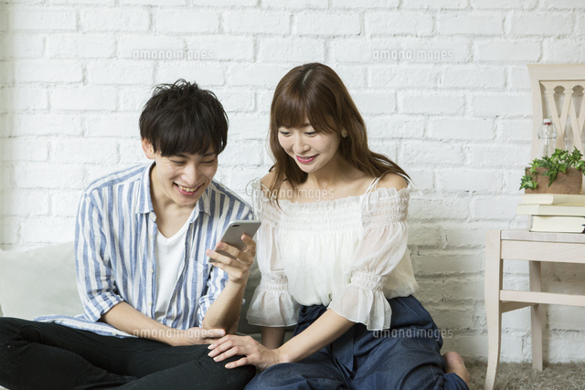 スマホを覗く笑顔の代カップル の写真素材 イラスト素材 アマナイメージズ