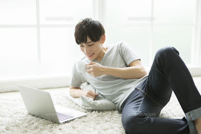 部屋でくつろぎながらパソコンを操作する代男性 の写真素材 イラスト素材 アマナイメージズ