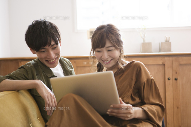 ソファに座りパソコンを見る笑顔の代男女 の写真素材 イラスト素材 アマナイメージズ