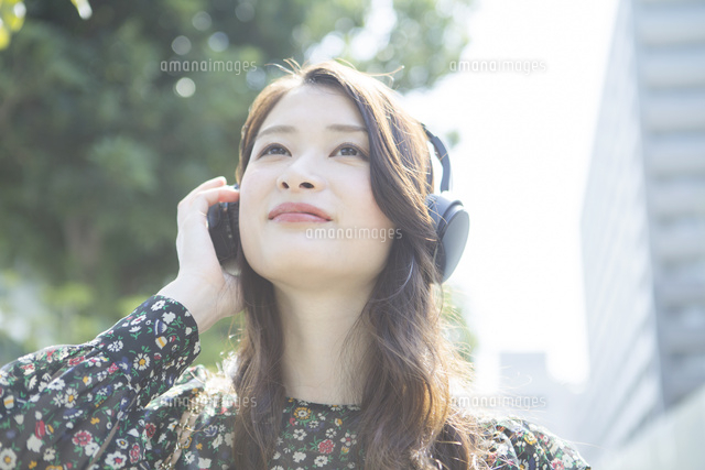 ヘッドホンに手を当てる笑顔の代女性 の写真素材 イラスト素材 アマナイメージズ