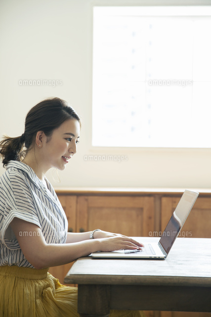 窓際でパソコンを操作する笑顔の代女性の横顔 の写真素材 イラスト素材 アマナイメージズ