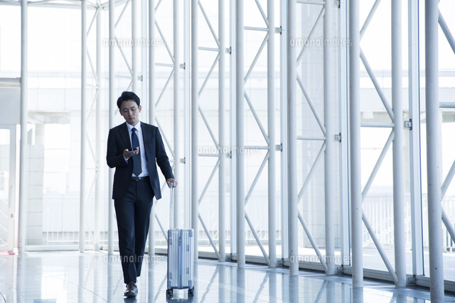 キャリーケースを持ちスマホを見るスーツ姿の代男性 の写真素材 イラスト素材 アマナイメージズ