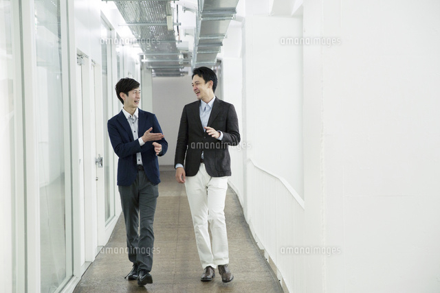 廊下で歩きながら話す代男性 の写真素材 イラスト素材 アマナイメージズ