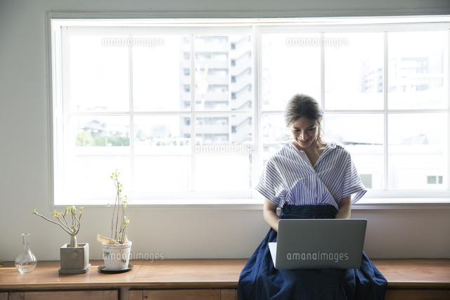 窓際でノートパソコンを操作する笑顔の代女性 の写真素材 イラスト素材 アマナイメージズ