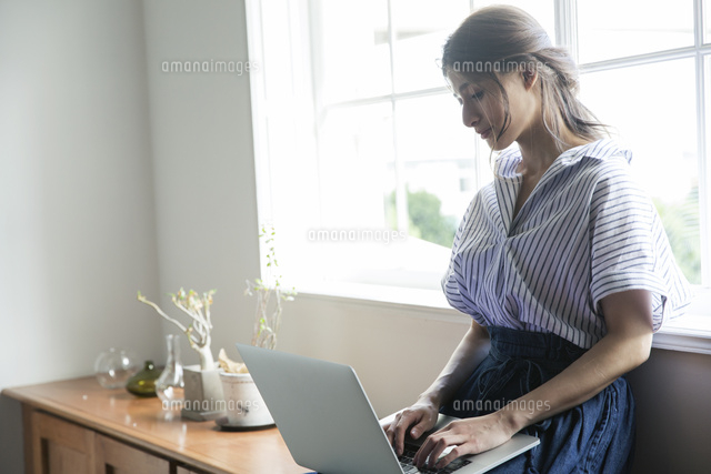 窓際でノートパソコンを操作する代女性 の写真素材 イラスト素材 アマナイメージズ