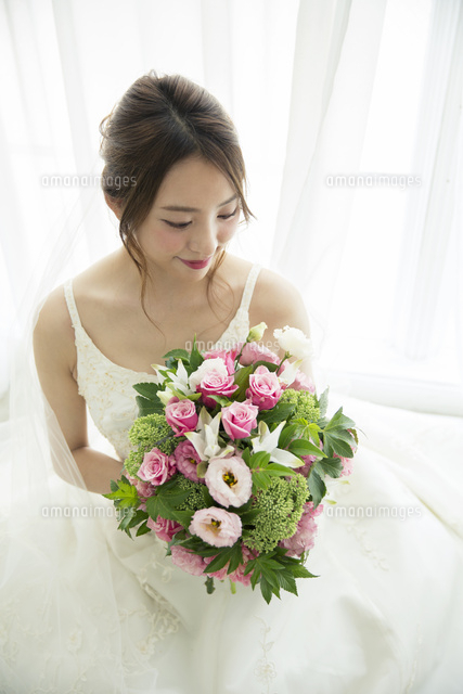 窓際に座りブーケを見つめるウエディングドレス姿の代女性 の写真素材 イラスト素材 アマナイメージズ