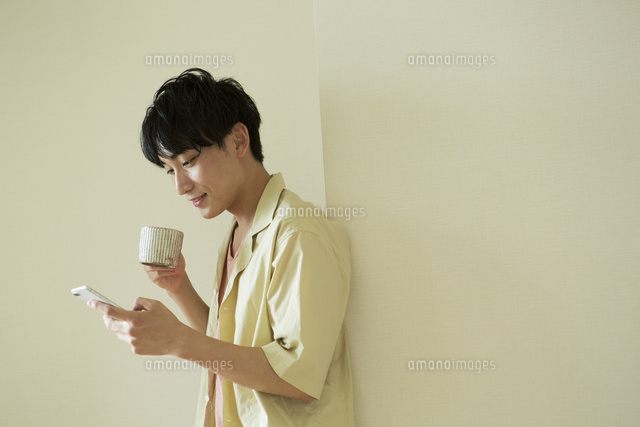 部屋でスマホをみながらくつろぐ代男性 の写真素材 イラスト素材 アマナイメージズ