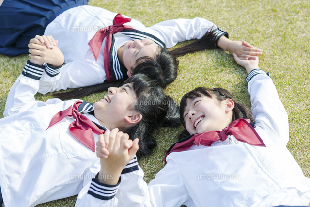 芝生に寝転んで手を繋ぐ女子校生 の写真素材 イラスト素材 アマナイメージズ