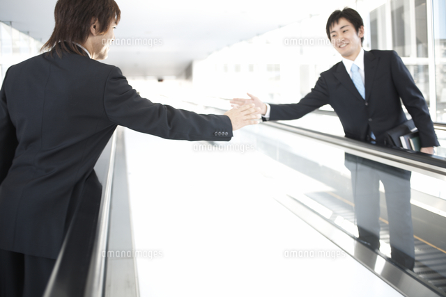 動く歩道で挨拶を交わすビジネスマン2人 の写真素材 イラスト素材 アマナイメージズ