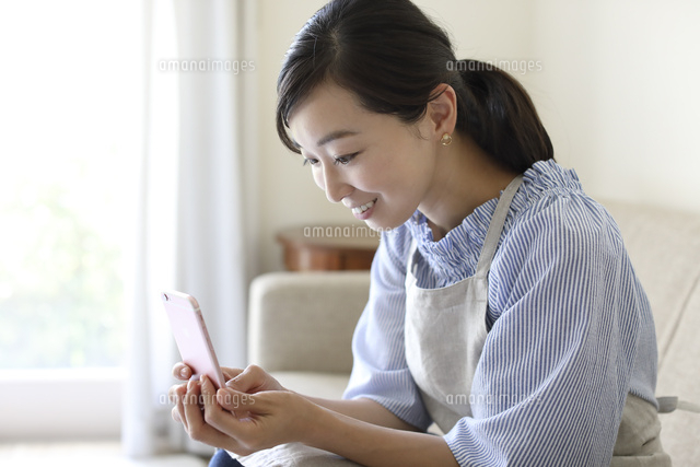 ソファーに座りスマホを見る女性 の写真素材 イラスト素材 アマナイメージズ