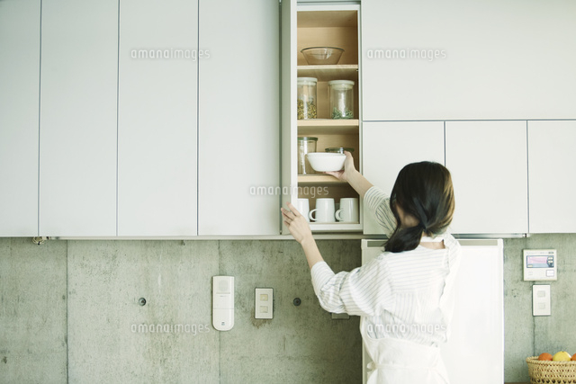 キッチンに立ち食器棚を開ける女性 の写真素材 イラスト素材 アマナイメージズ
