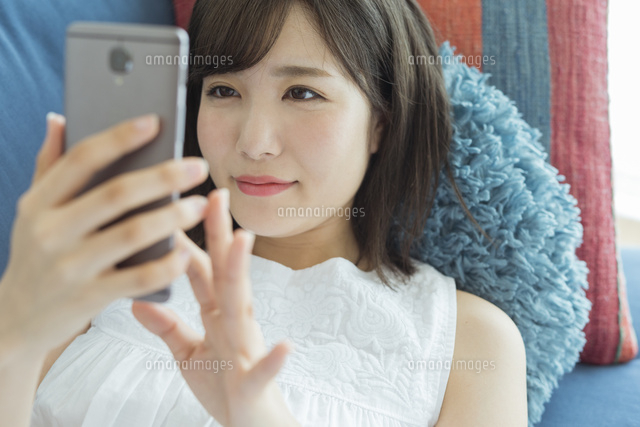 横になってスマートフォンを操作する女性 の写真素材 イラスト素材 アマナイメージズ