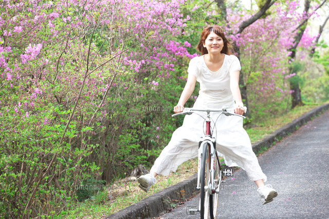新緑の中自転車で坂を下るする若い女性[10990000120]の写真・イラスト 
