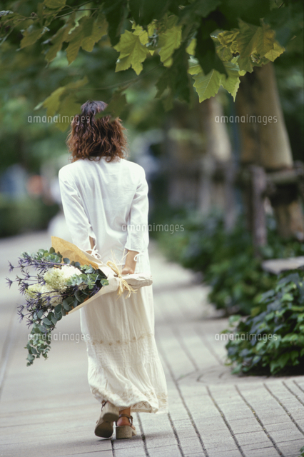 花束を持って歩く女性の後姿[10990008702]の写真・イラスト素材 