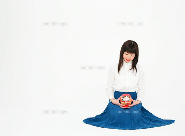 だるまを持ってうつむく女性 の写真素材 イラスト素材 アマナイメージズ