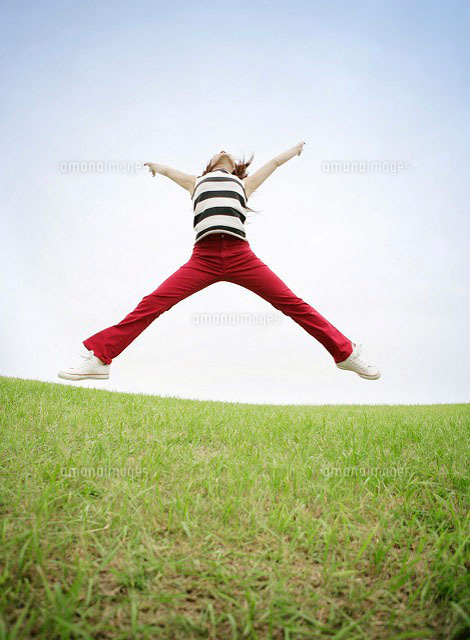 草原で飛び跳ねながら両手両足を大きく広げる女性 の写真素材 イラスト素材 アマナイメージズ