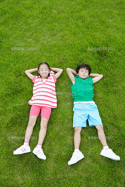 芝生で寝転ぶ二人の子供 の写真素材 イラスト素材 アマナイメージズ