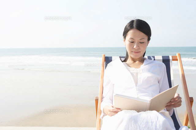 ビーチチェアに座り読書をする女性 の写真素材 イラスト素材 アマナイメージズ