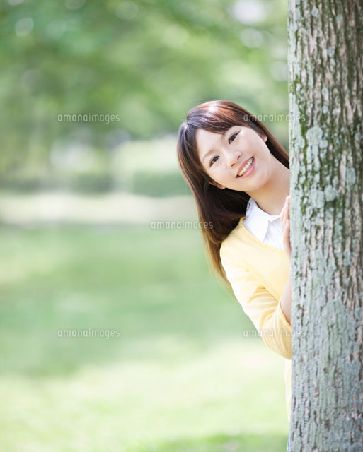 木の陰から顔を出す女性 の写真素材 イラスト素材 アマナイメージズ