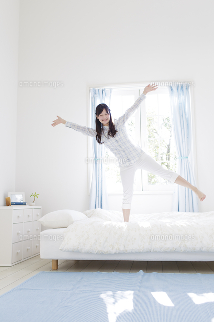 ベッドの上で両手を広げて立つ女性[11004103893]の写真・イラスト素材