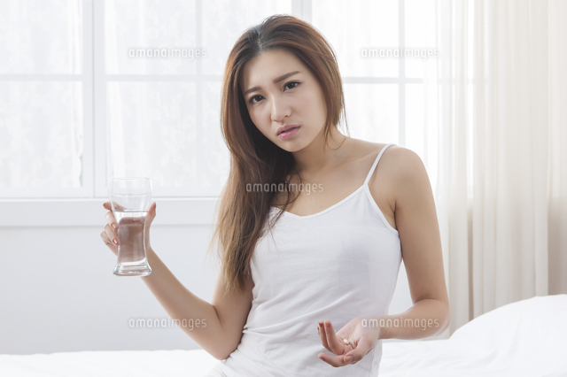 Young woman holding a glass of water trying to take a pill and looking ...