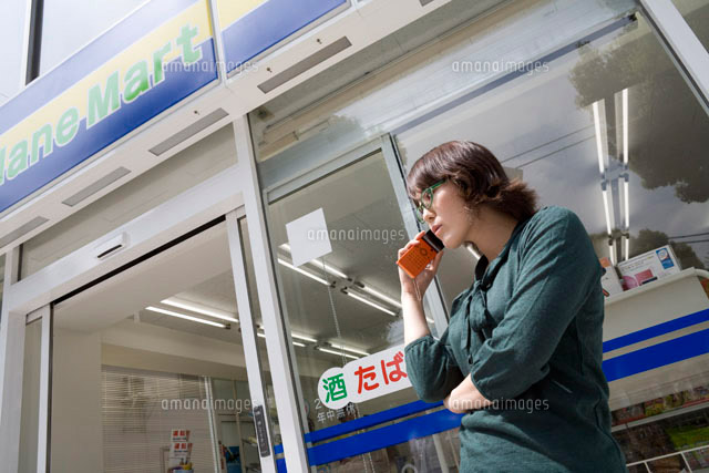 コンビニの外で携帯電話を使う女性 の写真素材 イラスト素材 アマナイメージズ