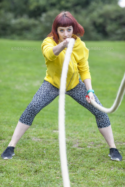 Young woman pulling rope on field[11015268811]の写真素材・イラスト素材｜アマナイメージズ