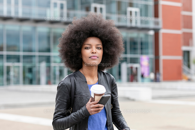Young Woman With Afro Hair In City Holding Smartphone And Takeaway Coffee Portrait の写真素材 イラスト素材 アマナイメージズ