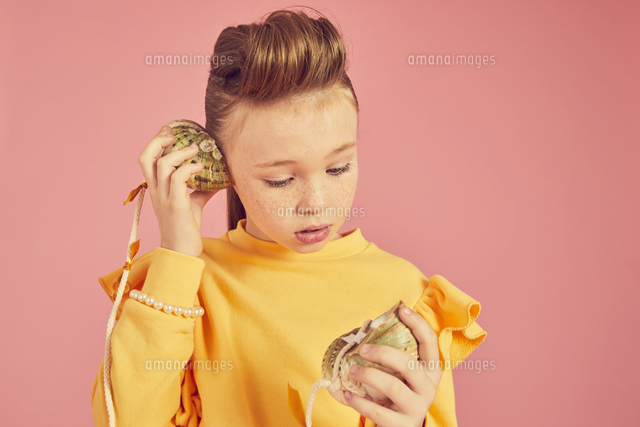 Portrait Of Brunette Girl Wearing Yellow Top Holding Sea Shell Phone On Pink Background の写真素材 イラスト素材 アマナイメージズ