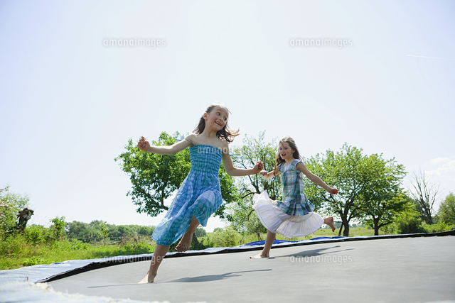Playful Carefree Barefoot Girls In Dresses Playing On Trampoline In Sunny Backyard の写真素材 イラスト素材 アマナイメージズ