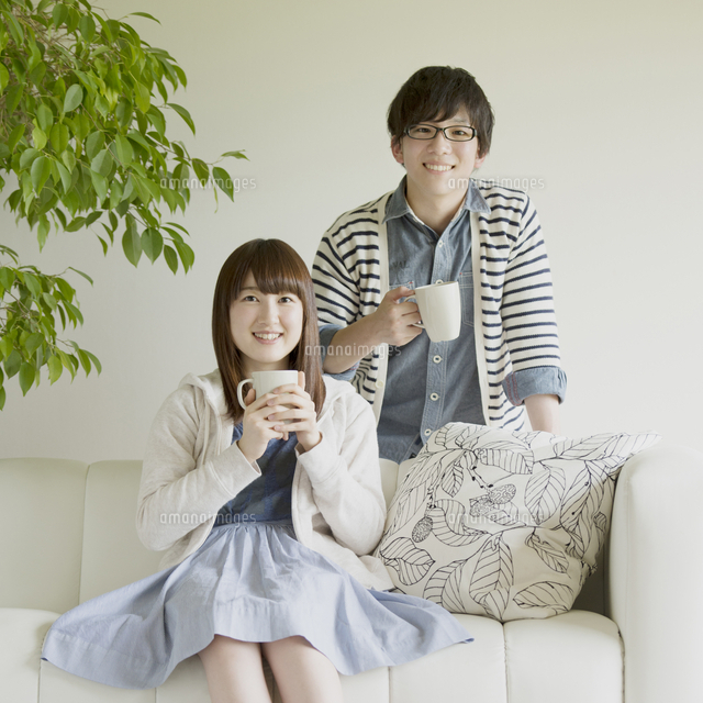 ソファに座りコーヒーを飲むカップル の写真素材 イラスト素材 アマナイメージズ
