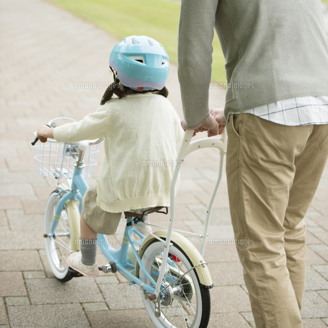 自転車の練習をする女の子と父親の後姿 の写真素材 イラスト素材 アマナイメージズ