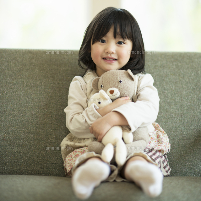 ソファーでぬいぐるみを抱き微笑む女の子 の写真素材 イラスト素材 アマナイメージズ