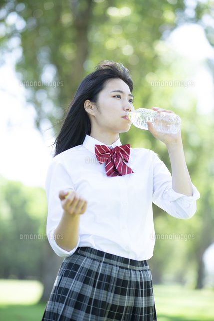 ポプラ並木で水分補給をする女子学生 の写真素材 イラスト素材 アマナイメージズ