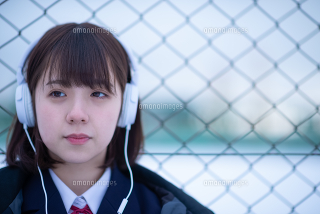 フェンスに寄りかかり音楽を聴く女子学生 の写真素材 イラスト素材 アマナイメージズ