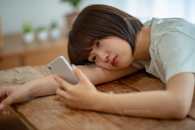スマホを見ながら落ち込む若い女性 の写真素材 イラスト素材 アマナイメージズ