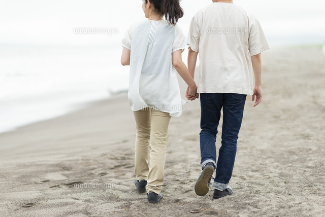 手をつないで海辺を歩くカップルの後ろ姿 の写真素材 イラスト素材 アマナイメージズ